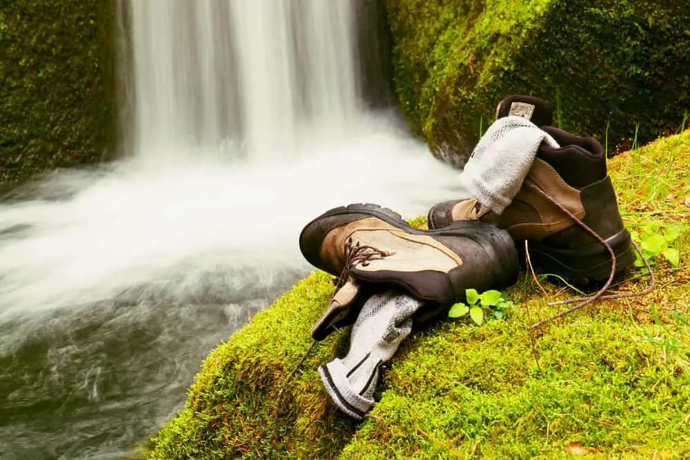Hiker high boots and sweaty grey socks. Resting on the mossy boulder at the nice mountain stream